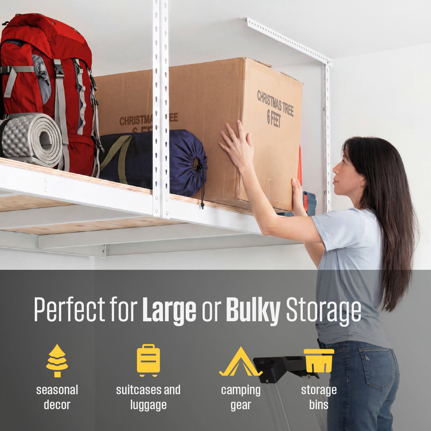 A woman pushes a large cardboard storage box onto a white overhead rack with plywood decking. A red backpack and other camping gear are visible on the rack, with text at the bottom reading 'Perfect for Large or Bulky Storage' and listing use cases like seasonal decor, suitcases and luggage, camping gear, and storage bins.