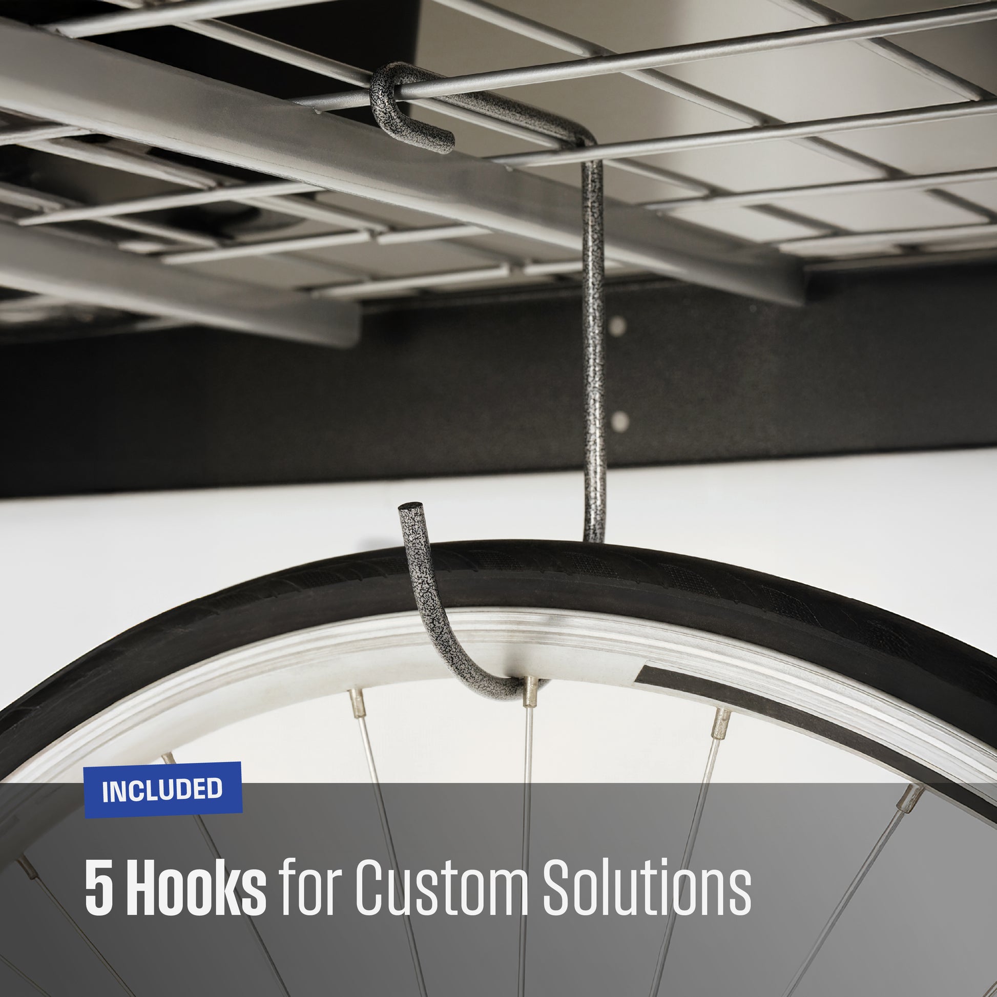 Close-up of a textured grey metal hook hanging from a garage shelf, with a bicycle tire partially visible to demonstrate use. Text overlay reads 'INCLUDED 5 Hooks for Custom Solutions'.