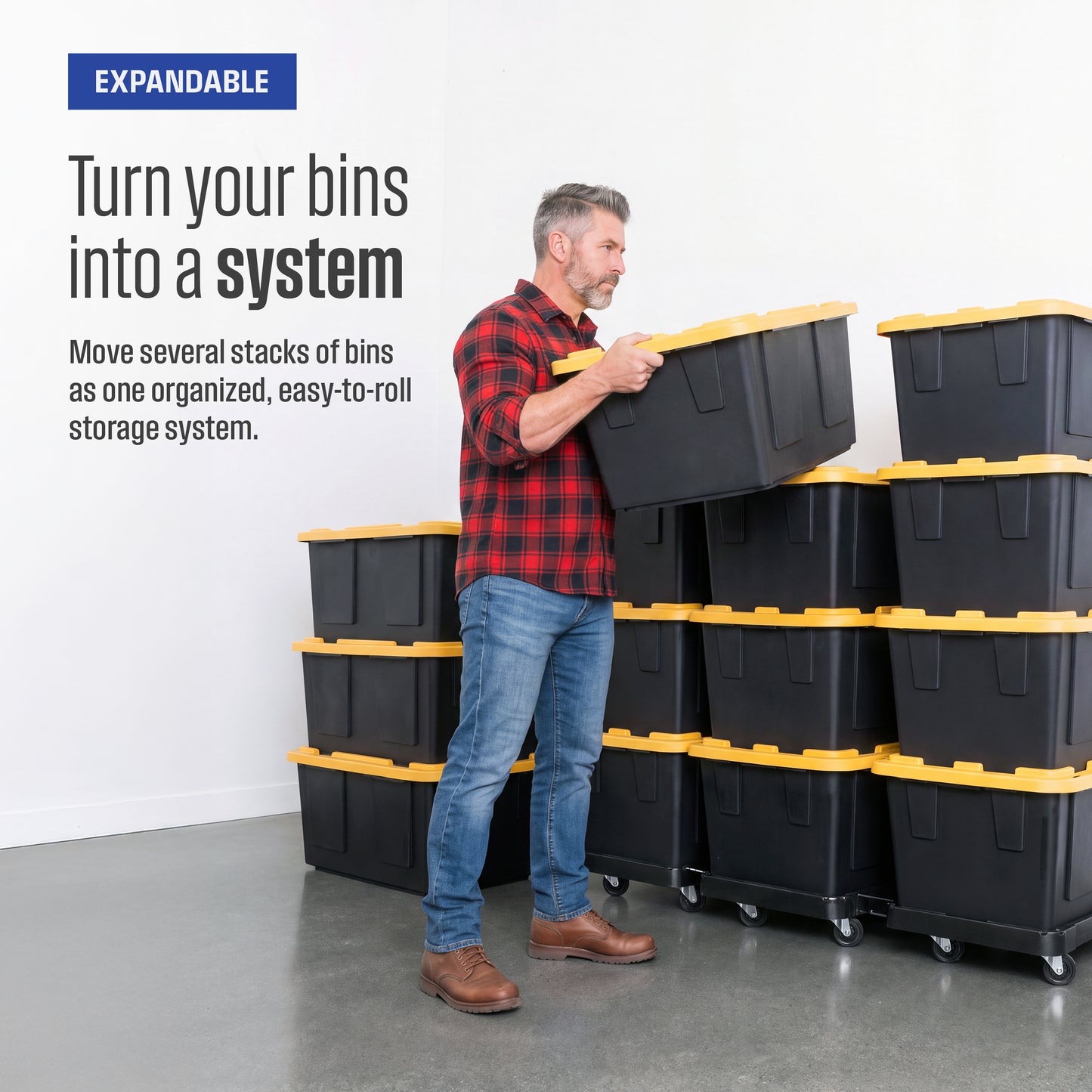 A man loads a black and yellow storage bin onto a stack of bins atop a bin dolly. A stack of similar bins is next to him. Text reads 'Expandable, turn your bins into a system, move several stacks of bins as one organized, easy-to-roll storage system'