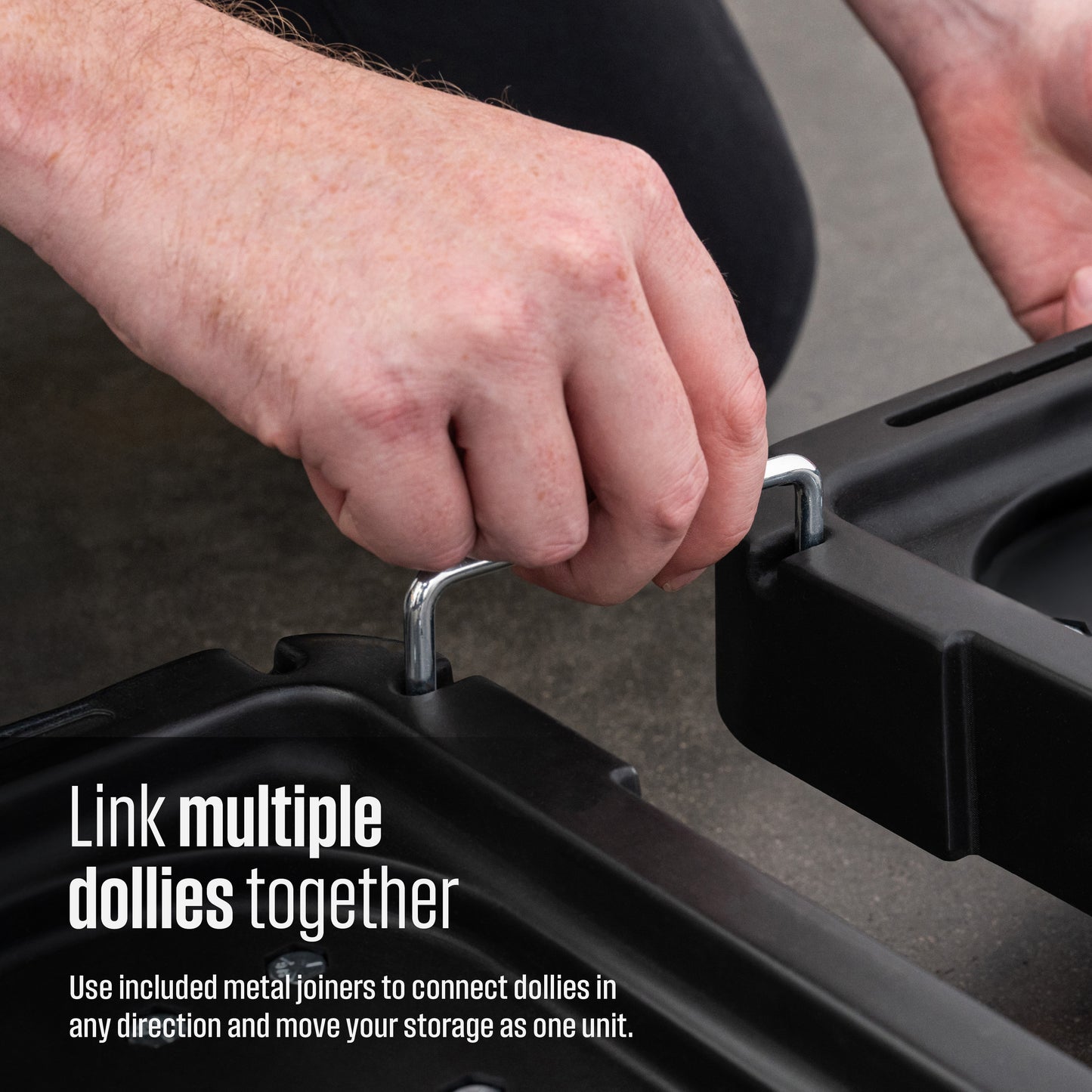 Close-up of a person's hands connecting black plastic storage dollies with silver metal joiners. Text overlay reads 'Link multiple dollies together, use included metal joiners to connect dollies in any direction and move your storage as one unit'